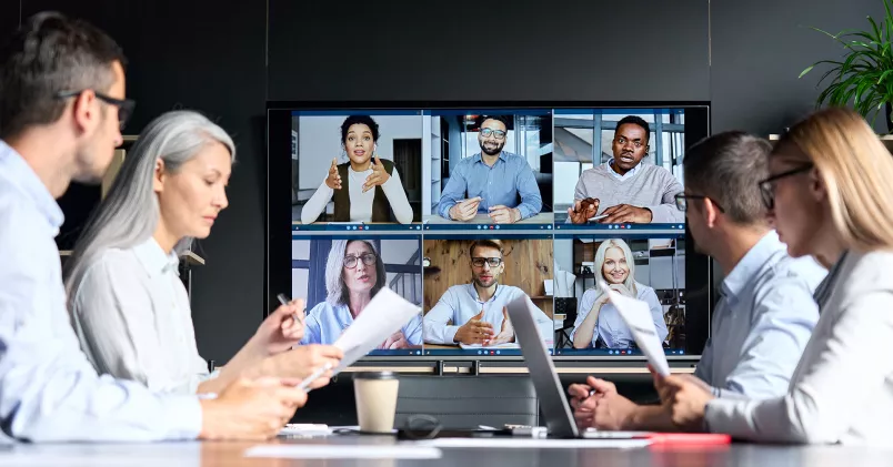 En grupp medarbetare har fysiskt möte och en annan grupp syns på skärm.