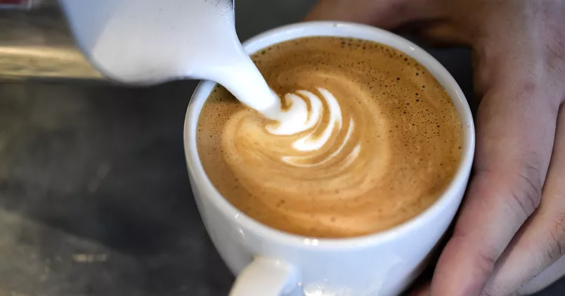 Skummad mjölk hälls upp i kaffekopp.