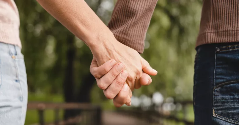 Par håller varandra i handen och promenerar i en park.