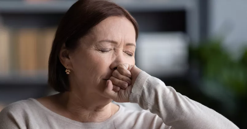 Kvinna ser ansträngd ut och för näven mot munnen.