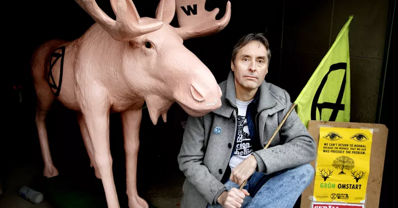 Klimataktivisten Pontus Bergendal håller i en flagga, omgiven av en rosa älg.