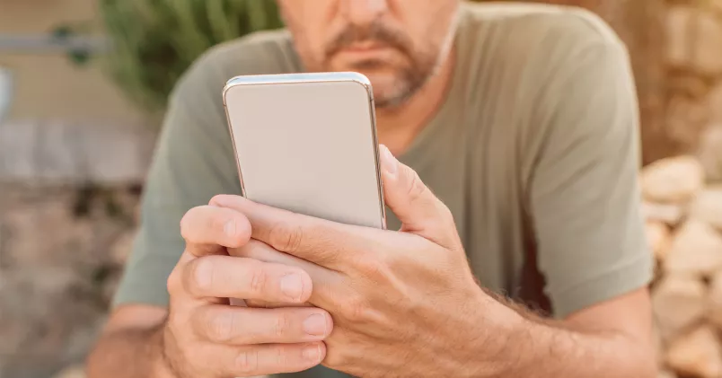 Man sitter utomhus och tittar i telefon.