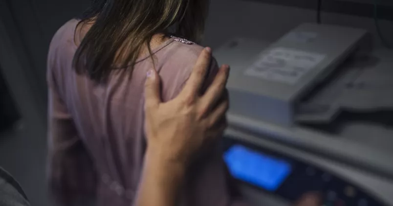 Man lägger sin hand på kvinna vid kopiator.