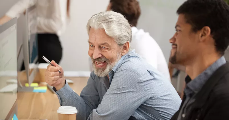 Att fortsätta jobba och samtidigt ta ut sin allmänna pension, och investera den i aktier, kan innebära ekonomiska risker. Man i senare delen av karriären sitter bredvid yngre man framför datorn.