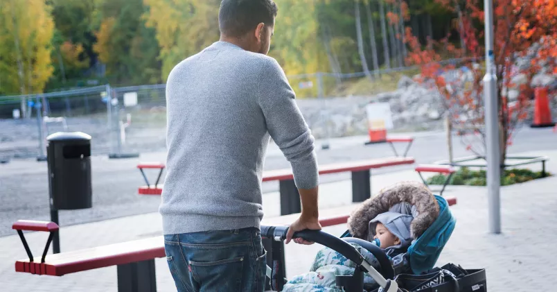 Pappa går med barnvagn vid lekpark.