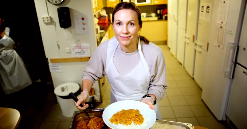 Gea Alsterberg i soppköket där hon serverar en tallrik mat iklädd ett förkläde.
