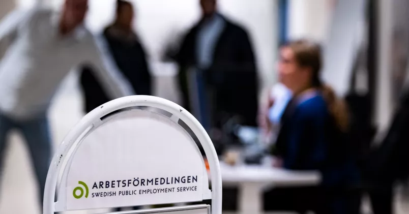 Människor i bakgrunden. I förgrunden e nskylt för Arbetsförmedlingen.