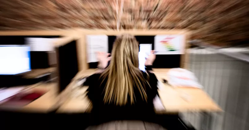 Stress på arbetet. En kvinna vid ett skrivbord. Suddigt och skakigt fotografi som ska symbolisera stress.