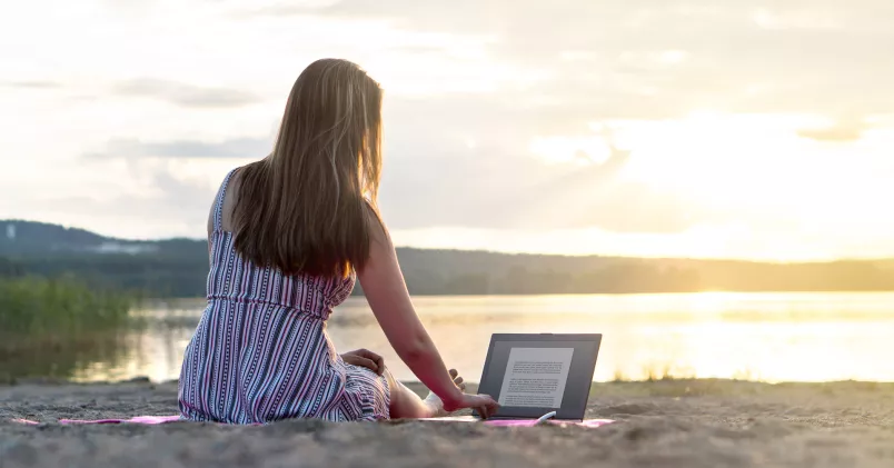 Kvinna på strand i solnedgången, arbetar på en bärbar dator.