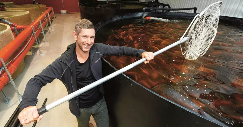 Johan Lundquist, vd på Gårdsfisk, med en hov i handen vid en stor fiskbassäng.