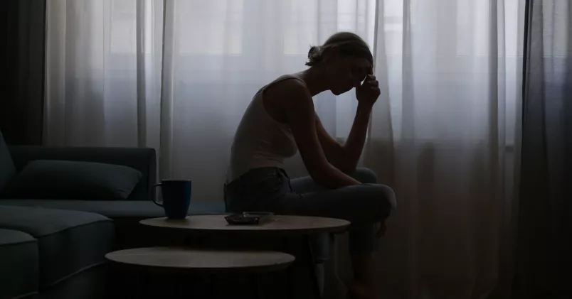 Migrän kvinna sitter i ett mörkt rum och tar sig för huvudet