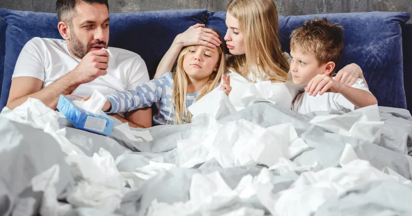 en familj ligger i sängen med snorpapper omkring sig