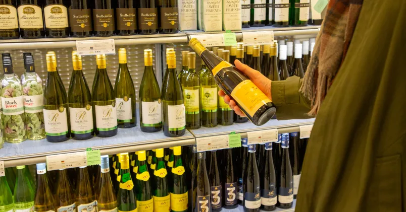 Ingen strejk på Systembolaget. På bilden en kund framför en hylla med vitvinsflaskor.