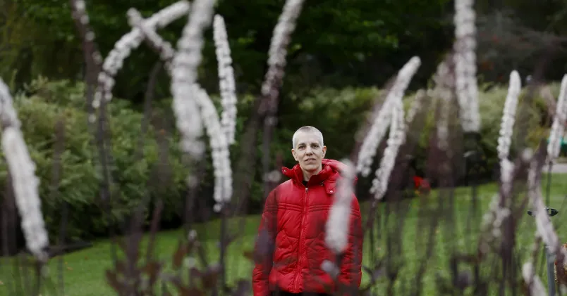  Maria Westin i röd jacka, hon står på avstånd i förgrunden svajar några vita växter.