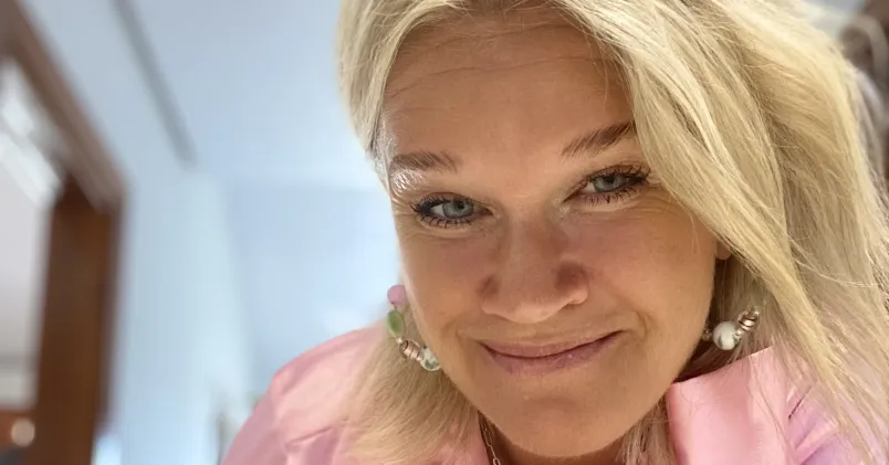 Tess Modig tittar in i kameran. Hon har långt blont hår och en rosa blus. Bakgrunden är lugn.