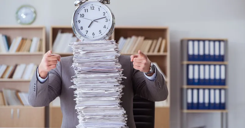 Pappershög på skrivbord och en klocka