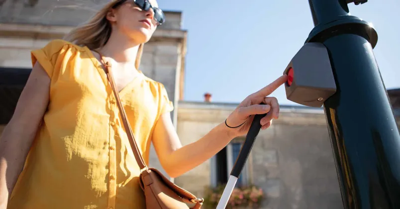 En person använder en tryckknapp i offentlig miljö, illustrerande tillgänglighet och hinder som tas upp i DO:s rapport om diskriminering av personer med funktionsnedsättning.