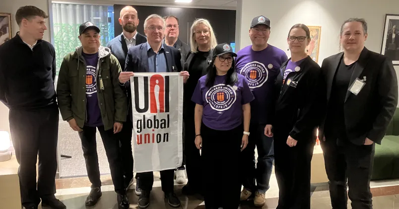 En grupp fackliga representanter från Workers United står inomhus och håller en banderoll med texten ”UNI Global Union”.