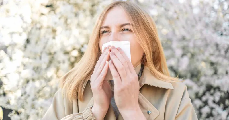 En kvinna snyter sig under ett blommande träd