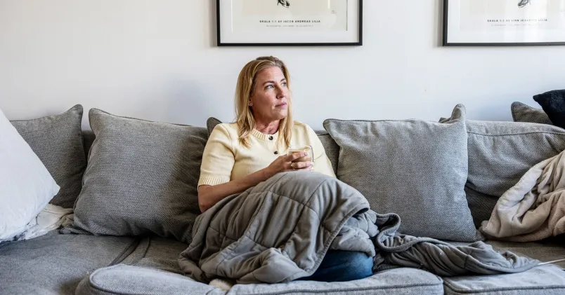 Hemmiljö med Jeanette Lilja i soffa och filt. Illustrerar situationen när barnet blir hemmasittare och vardagen stannar hemma.