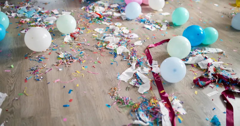 Ballonger, färgad konfetti, serpentiner och sönderrivet papper ligger utspridda på ett ljust golv efter en fest.