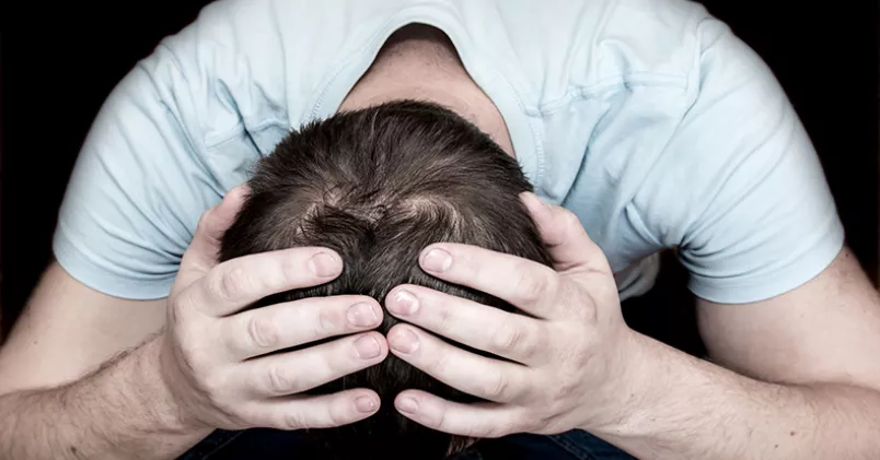 Man med händerna på sitt nedböjda huvud.
