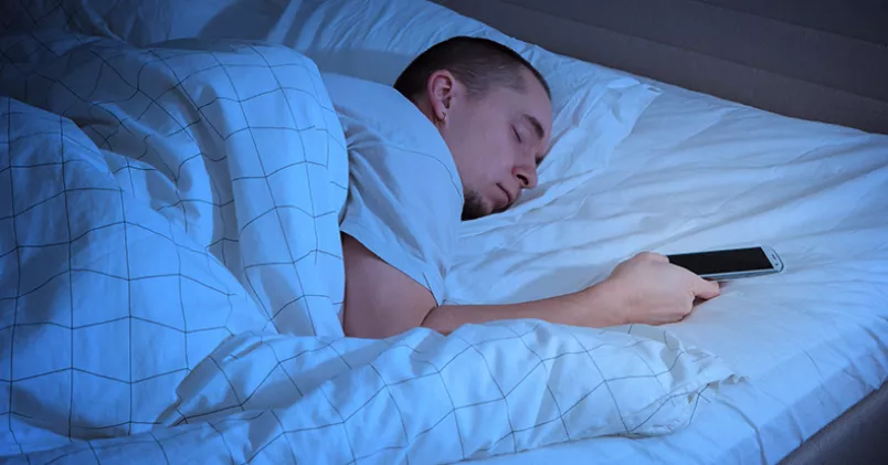 Man ligger och sover med mobilen i handen.