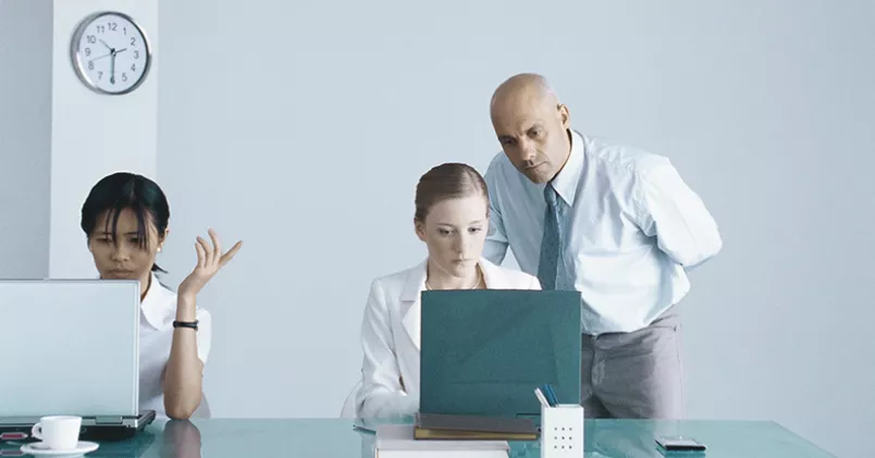 Man lutar sig över kvinna för att se vad hon gör på sin dator.