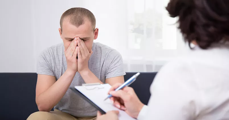 Man sitter med nedböjt huvud i samtal med kvinna som antecknar.