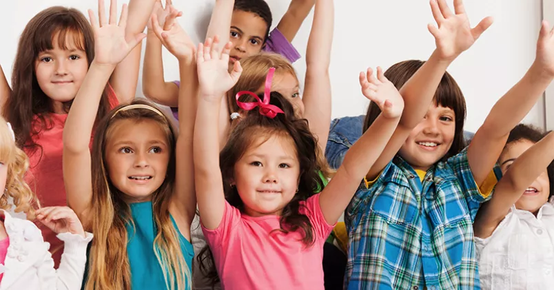 En grupp med barn sträcker händerna i luften.