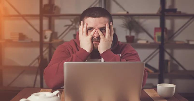 Man vid dator tar sig för ansiktet.