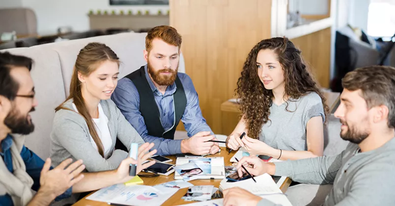 Unga människor sitter och jobbar runt ett bord.