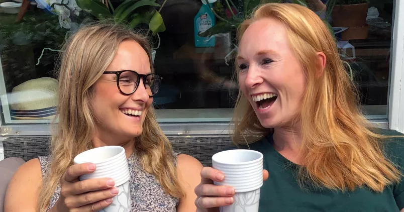 Två kvinnor som skrattar och dricker kaffe ihop.