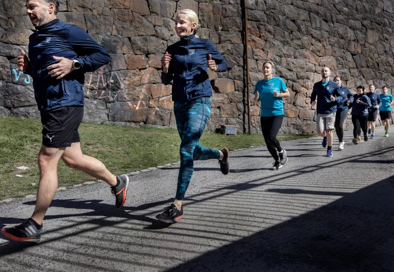 Löpare springer på rad utmed en stenmur.