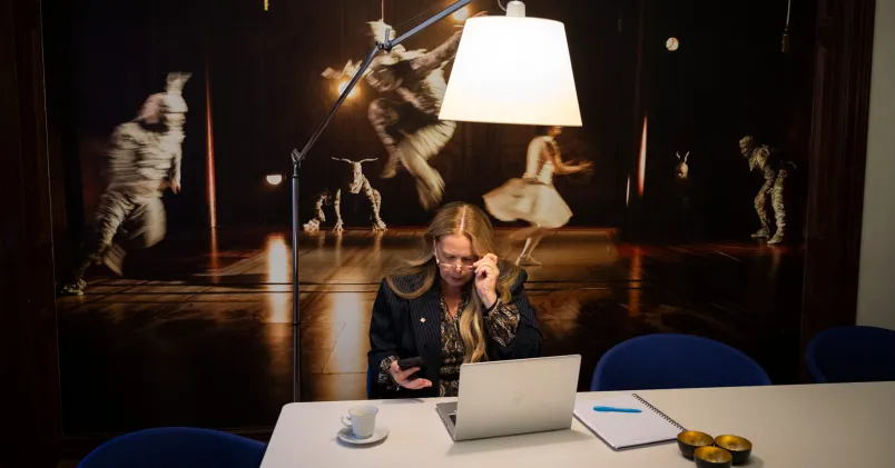 Petra Brylander, Vd och koncernchef Malmö stadsteater, sitter vid en bärbar dator med en mobiltelefon i handen. 