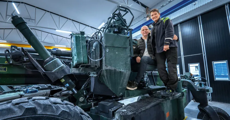 Ted och Magda Bucher arbetar tillsammans på Bofors testcenter står omfamnade framför ett militärt testfordon
