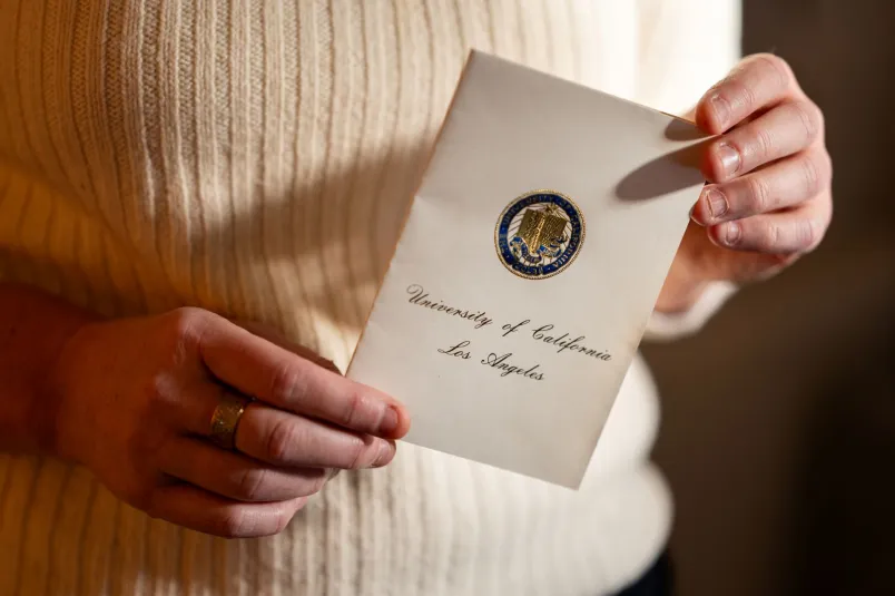 Maria Dahlins händer håller i en inbjudan till hennes examen på UCLA.