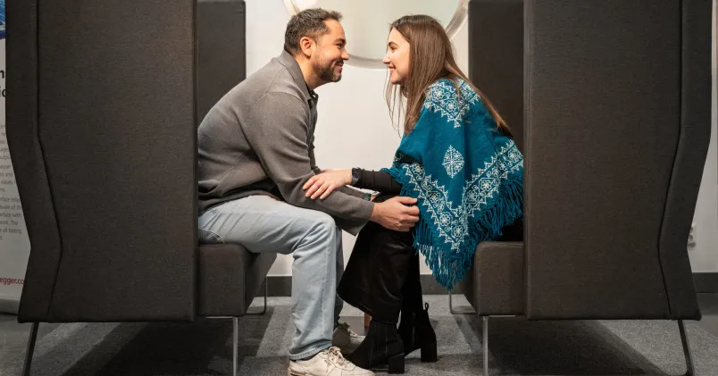 Två kollegor inom mjukvaruutveckling sitter tätt tillsammans i kontorsmiljö i en artikel om kärlek på jobbet.