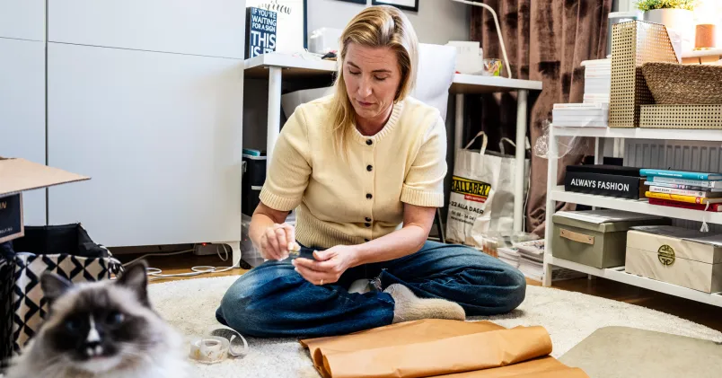 Jeanette Lilja i hemmiljö på golv med arbets-/pysselmaterial. Kopplar till flexibilitet och pauser i ett anpassat arbetsliv.