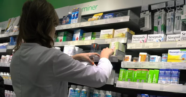 Apoteksanställd kvinna plockar upp varor på hylla.