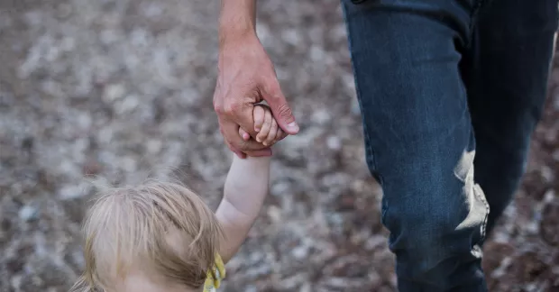 Närbild på man som håller sitt barn i handen.