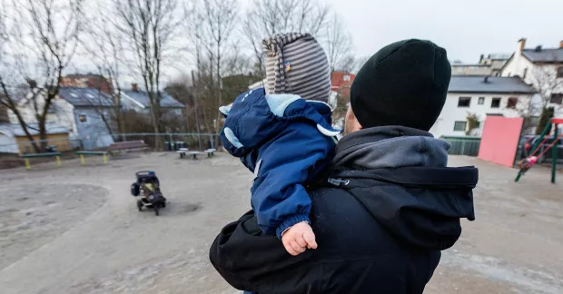 Pappa bär barn vid lekplats.