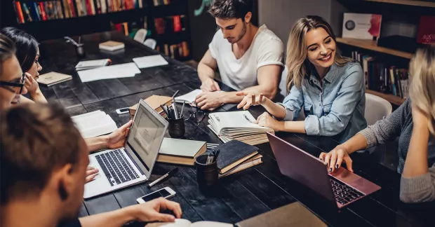 Studenter sitter runt bord med datorer.