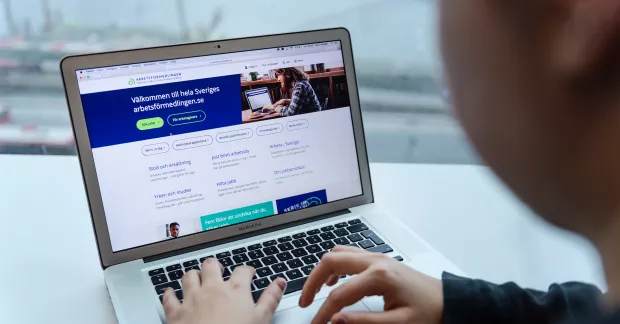 Man sitter vid dator och tittar på arbetsförnedlingens hemsida.