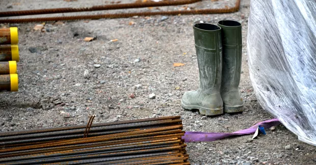 Byggarbetsplats. Armeringsjärn och rör på marken bredvid ett par tomma gummistövlar. 