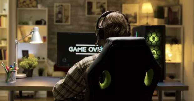 En man spelar PC-spel med en stor dator på bordet. Fotograferad bakifrån, sitter i en stol. 