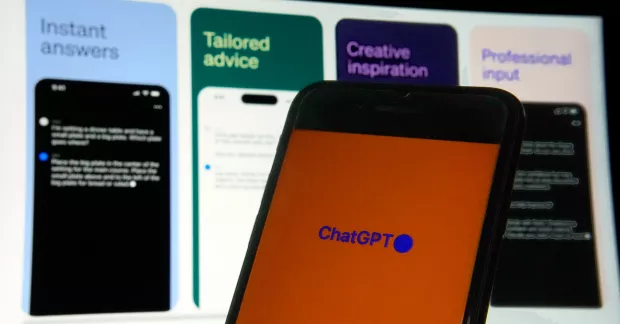 En mobiltelefon med ChatGPT öppet och en skärm i bakgrunden med olika AI-svar på dem.