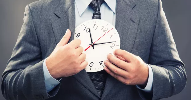 En man i kostym håller upp en äldre klocka med tim- och minutvisare. 