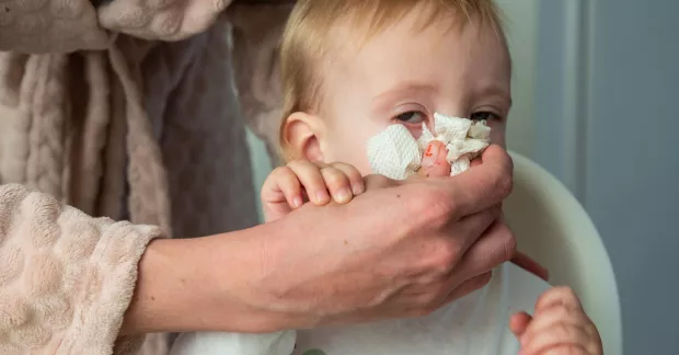 Kvinna torkar näsan på förkylt småbarn.