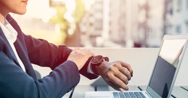 Kvinna vid dator kollar sitt armbandsur.